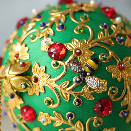 A close up of a handmade push pin ornament showing a small gold bee charm pinned to a satin ball with dressmaker pins by Whim5season.