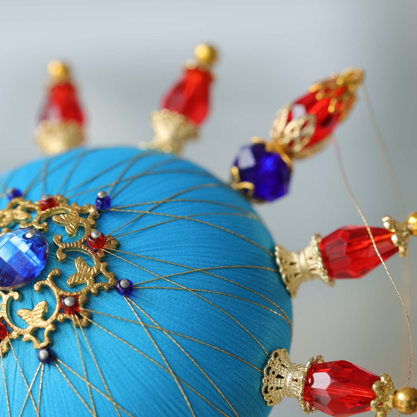 Close-up of a decorative blue satin foam base with gold and red embellishments attached with dressmaker push pins by Whim5seasons.