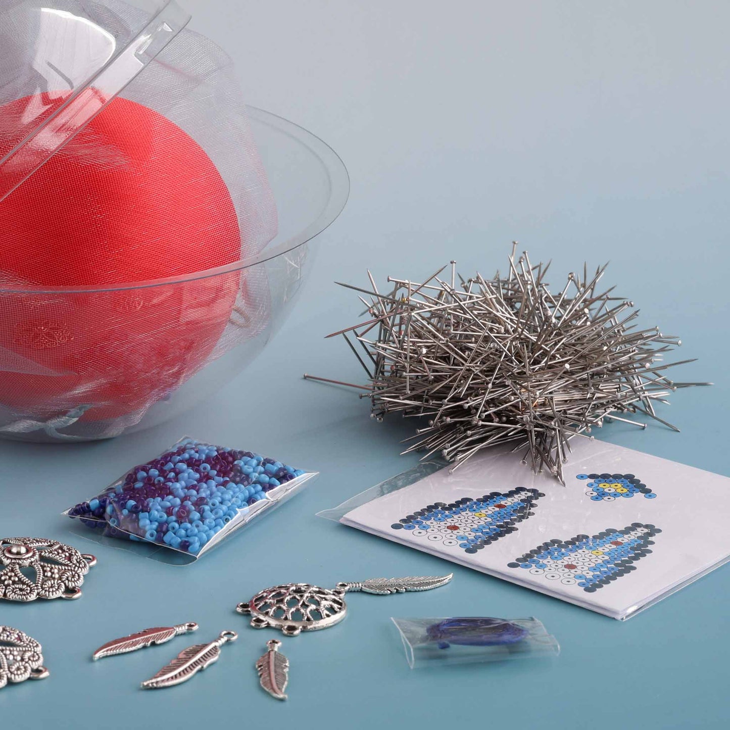 Crafting supplies for making a satin push pin ornament, including a red satin ball, pins, beads, paper patterns, and decorative elements by Whim5seasons.