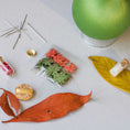 Load image into Gallery viewer, Push Pin Ornament includes these materials: assorted maple leaf charms, leaf ribbon, beads, and gold thread, on a light surface. (Olive)
