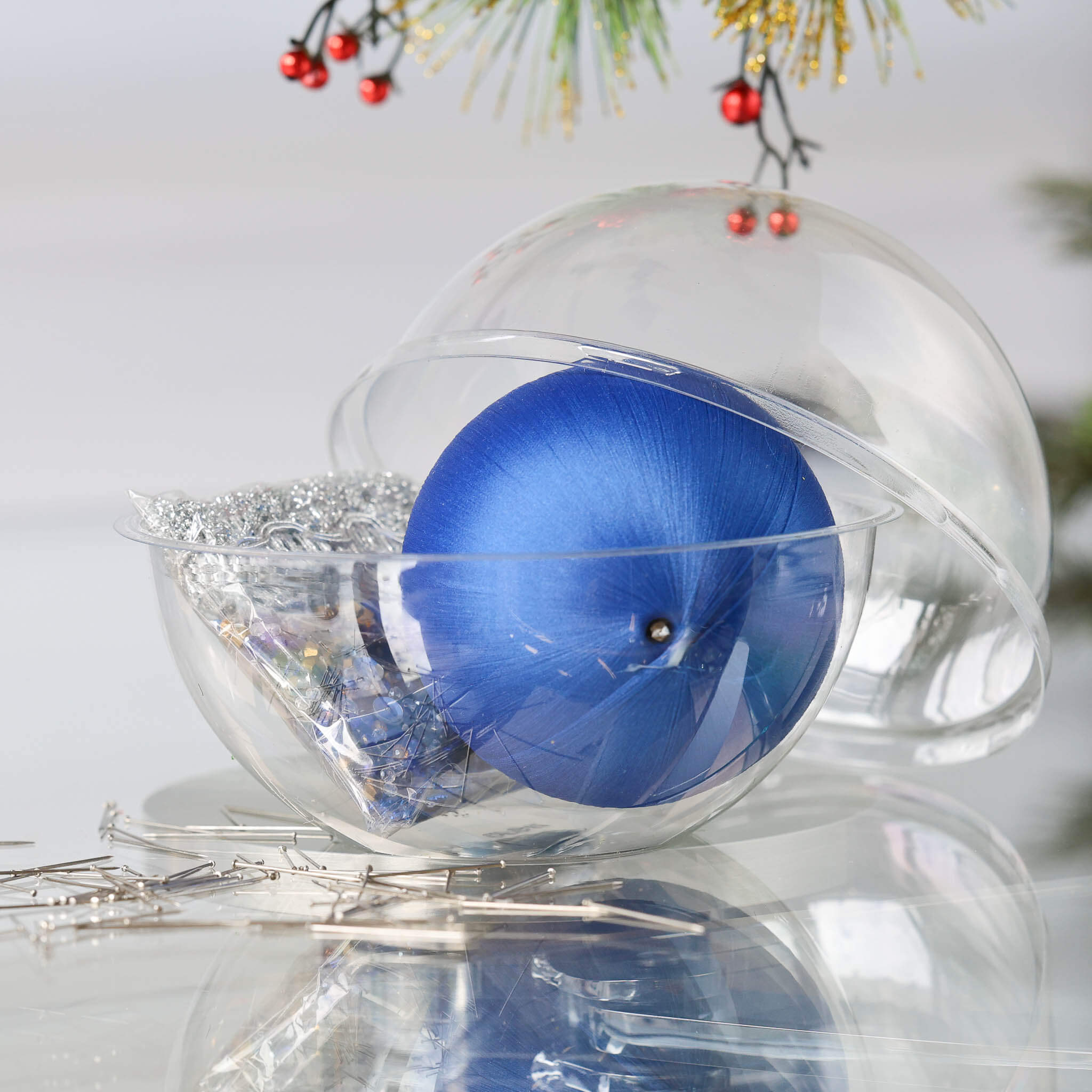 DIY Zima Ornament Kit includes: clear plastic container with a blue satin ball, silver trim, and dressmaker pins in a small clear bag on a white background. (Blue)