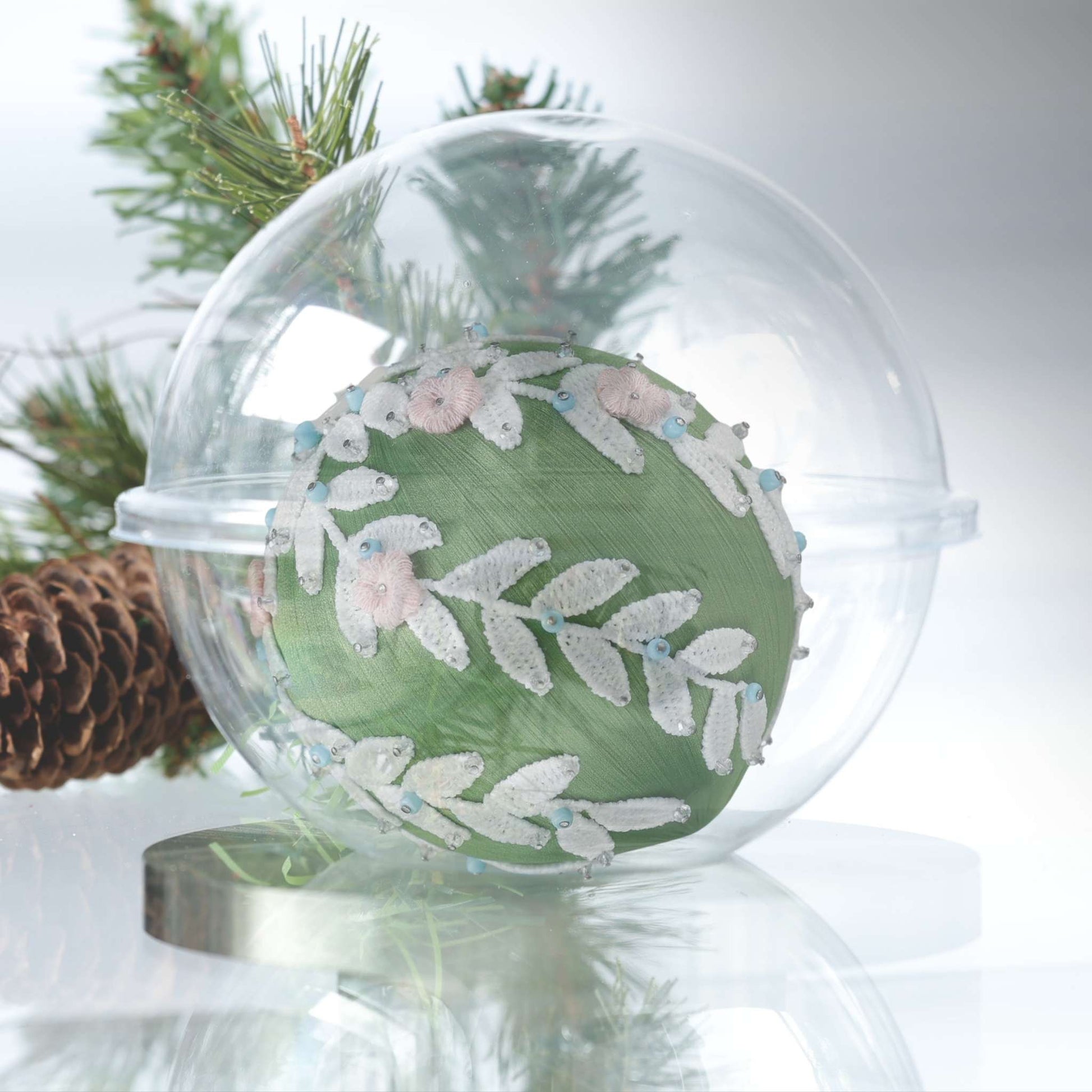 DIY Frosted Laurel Ornament Kit shows a clear round container with a green satin ball, and push pin kit materials in a small clear bag on a white background with Christmas greenery by Whim5seasons.