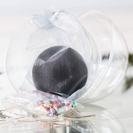 Push Pin Ornament Kit comes in a clear plastic container with  a black satin ball, tiny colorful jingle bells, and star sequins in a small clear bag, set against a white background.