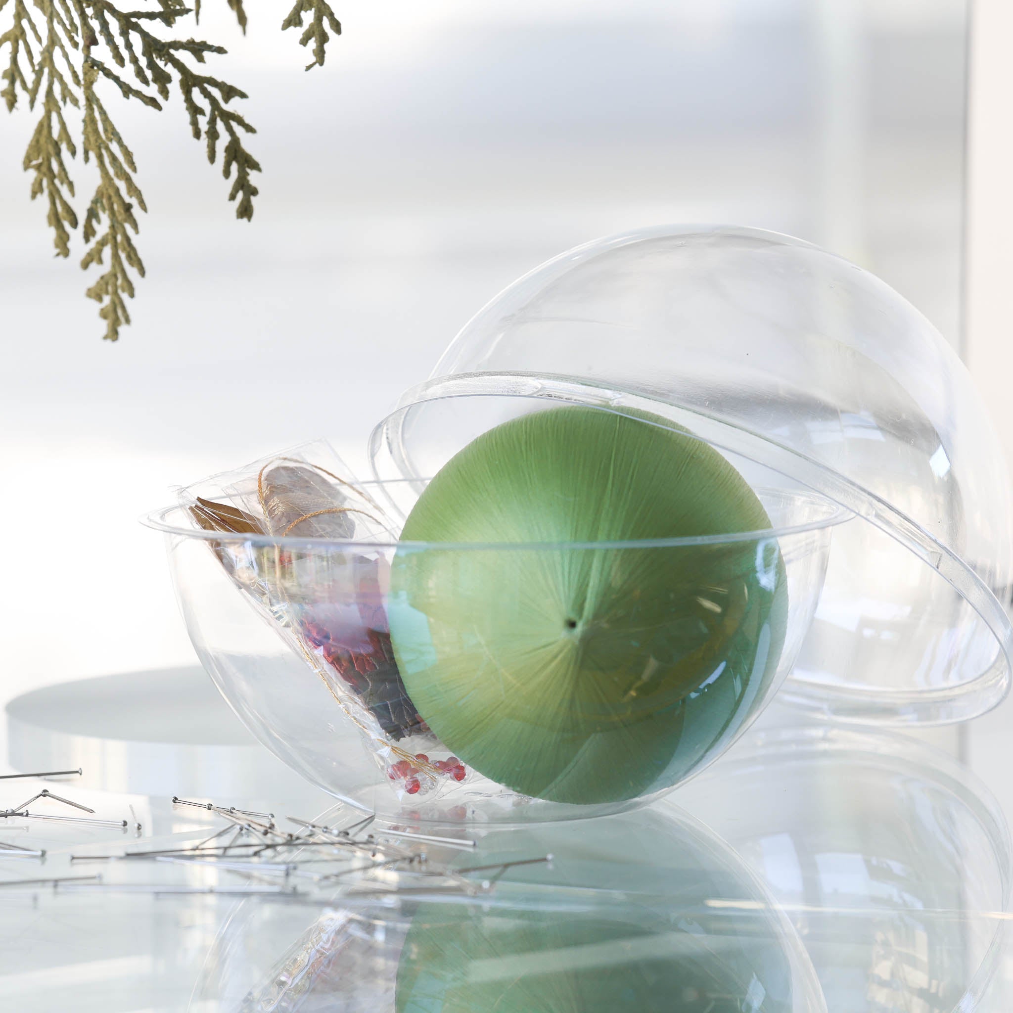 Materials for Push Pin Ornament "Leaves Are Falling" in olive are inside a round plastic clear container and have an olive colored satin foam core and a bag with beads and charms. (Olive)