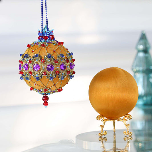 Two push pin satin ornaments of mustard color. One is handmade and finished Christmas ornament, and the other is on a gold stand .Completed push pin ornament features purple rhinestones, blue beads, and gold cording. (Gold)