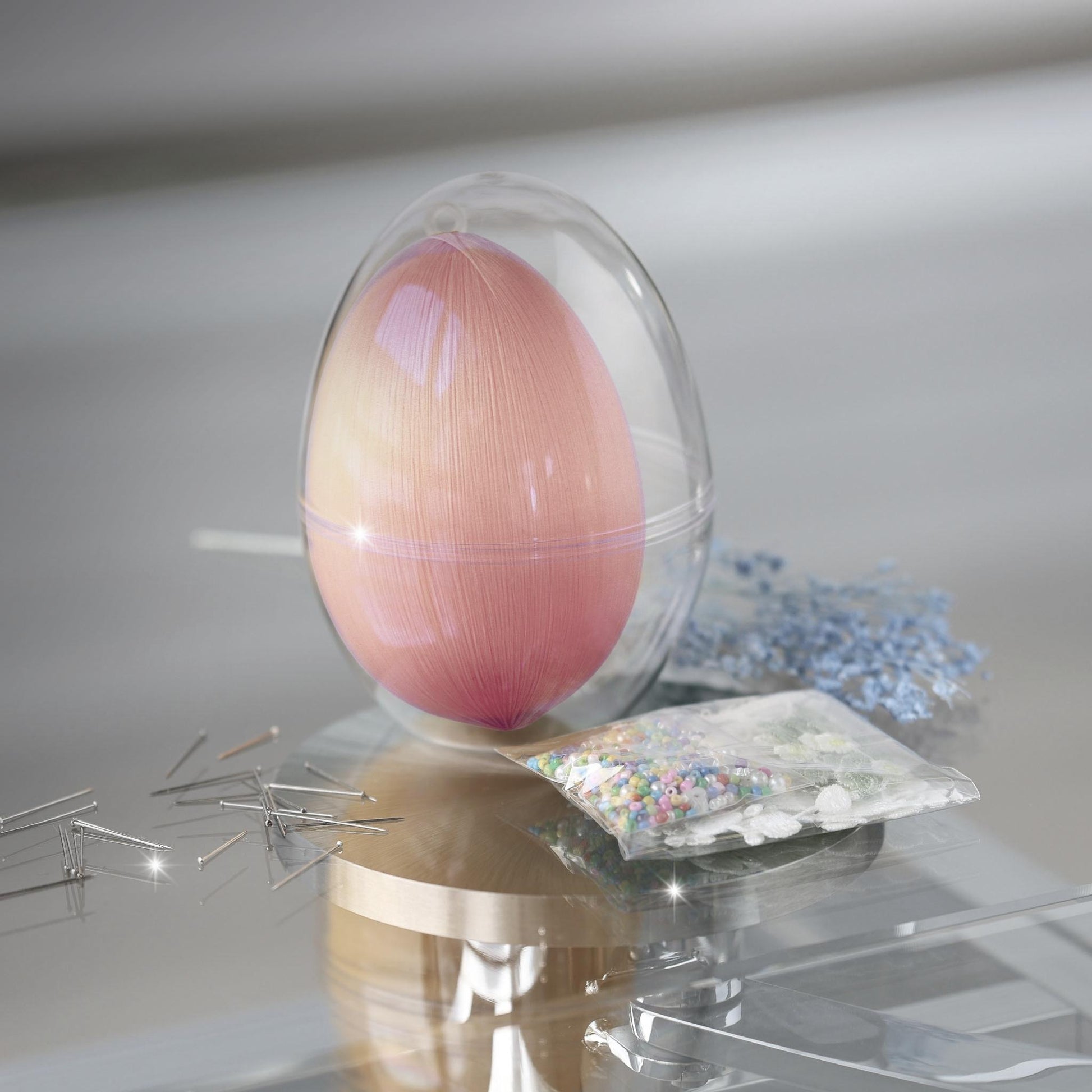 Clear plastic egg-shaped container with a satin bright yellow egg and a package of beads for a push pin project on a reflective surface by Whim5seasons.