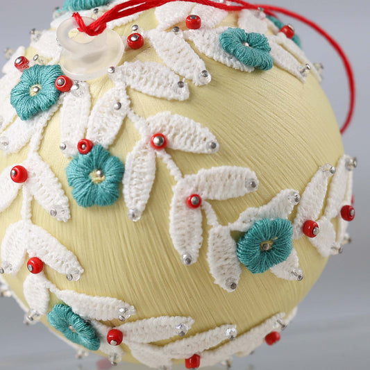 Close-up of a satin push pin ornament - a khaki-colored foam base with white lace, teal-colored flower embroidery patches, and clear glass seed beads. (Khaki)