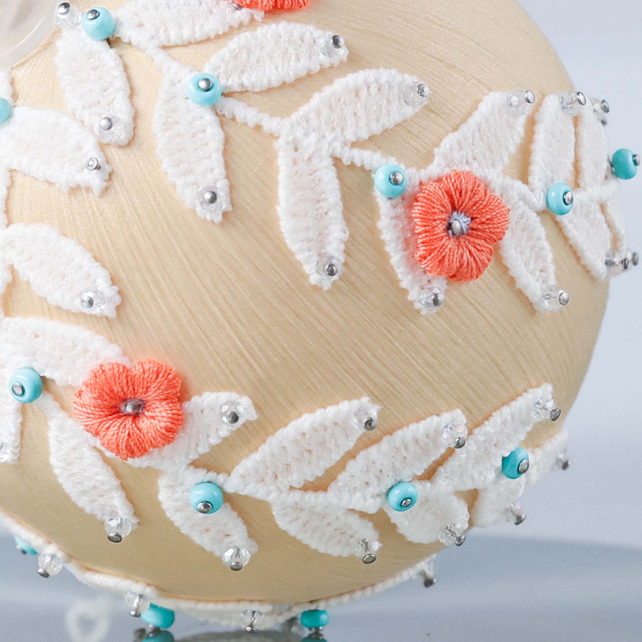 A picture of a part of a handmade push pin retro style Christmas ornament - while lace and orange flowers pinned on a satin ball with dressmaker pins. (Papaya Whip)