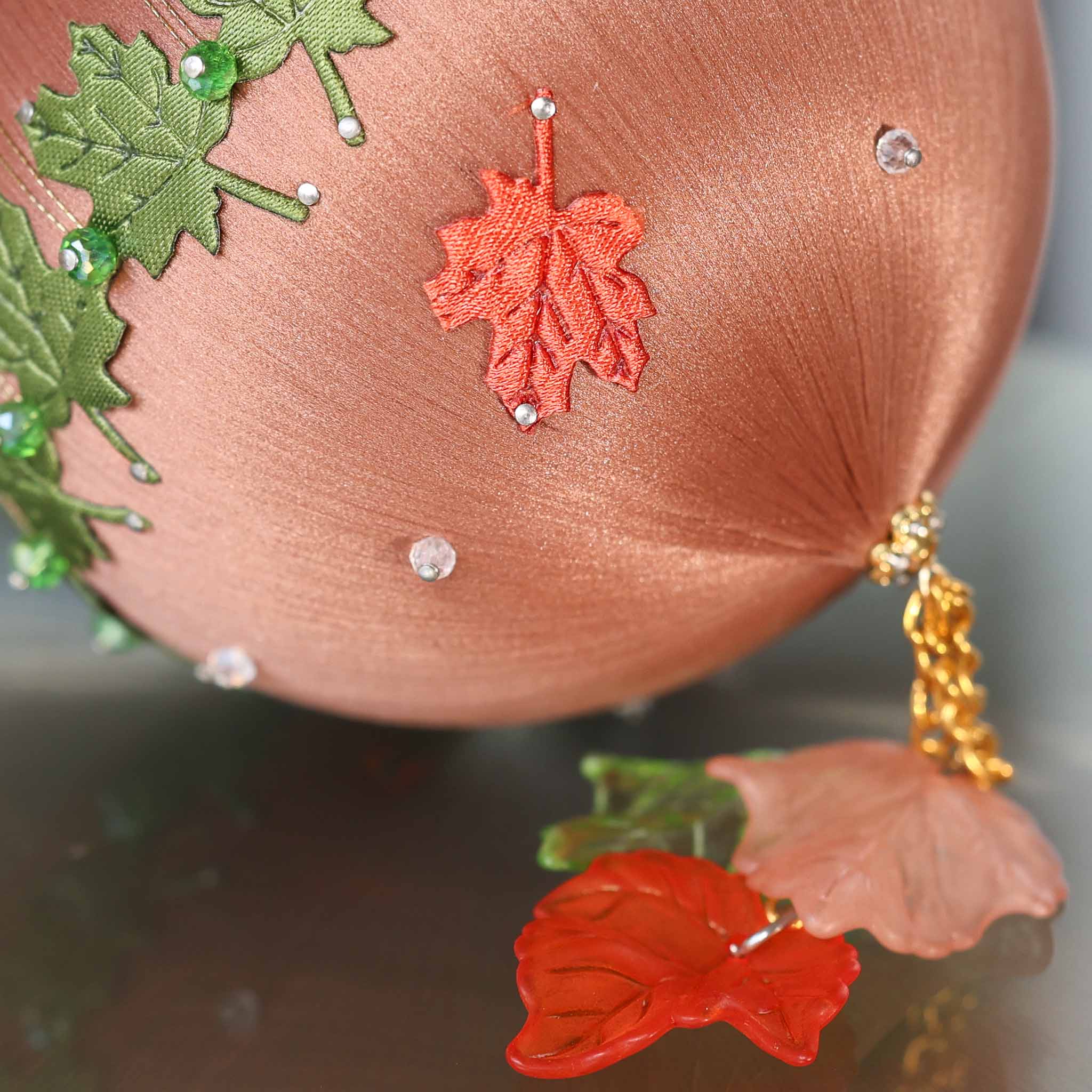 A close-up of a Handmade Push Pin Ornament in rosy brown featuring a rust colored fabric maple leaf applique pinned to a satin foam core with dressmaker pins. (RosyBrown)