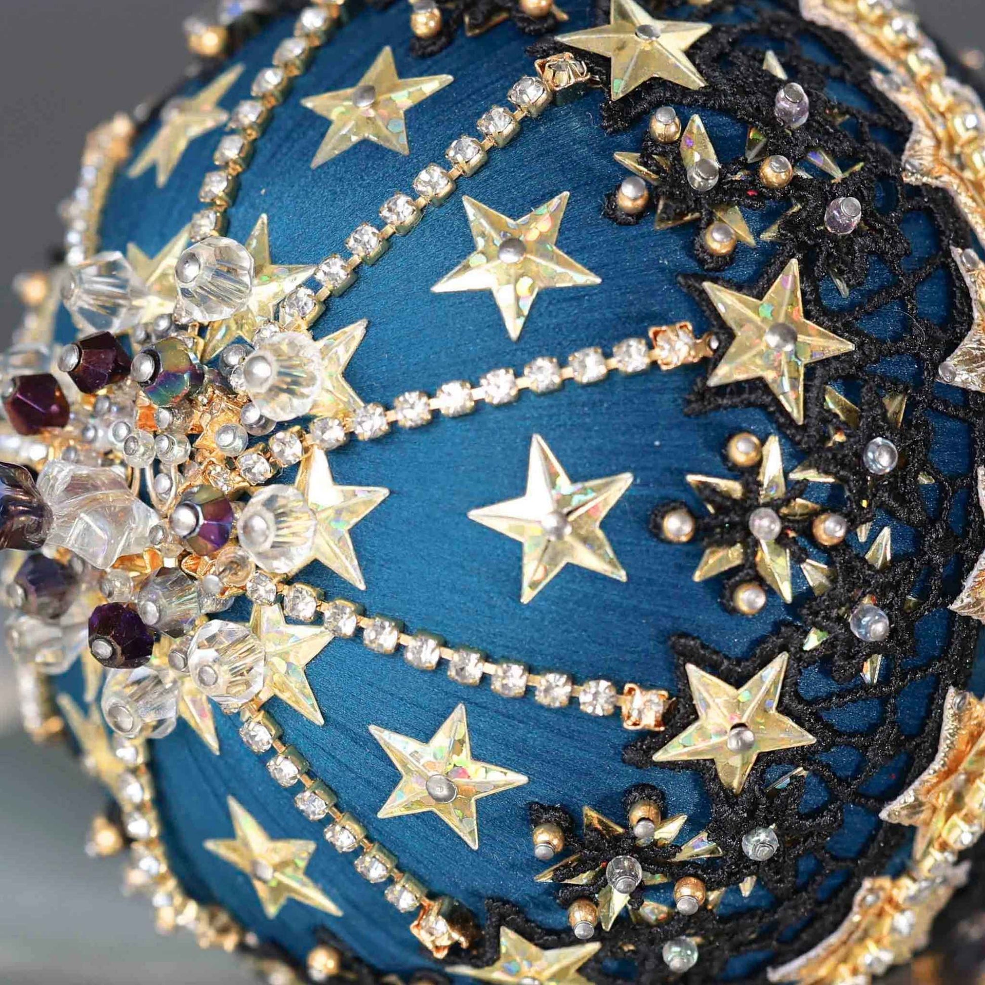 A close-up of dark purple beads and gold star-shaped sequins on a dark teal satin foam core ball featuring a completed handmade push pin ornament set against a dark gray background by Whim5seasons.