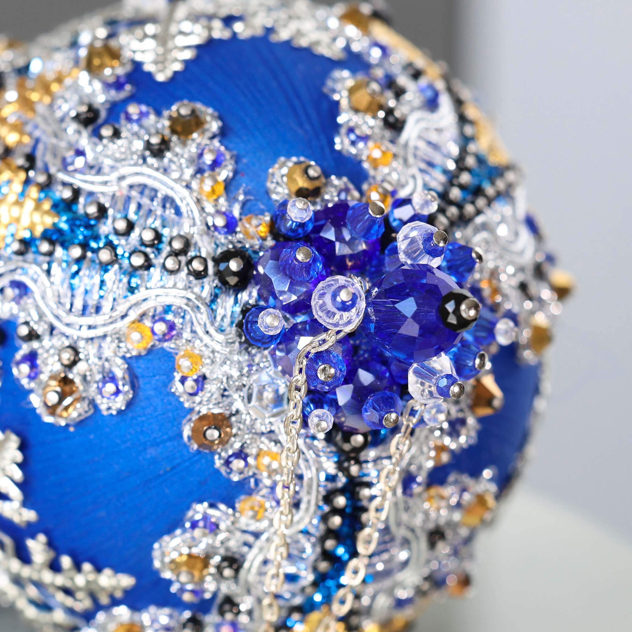 A close-up of a handmade push pin ornament's bottom with glass beads and metallic trim on a gray background.  (Blue)