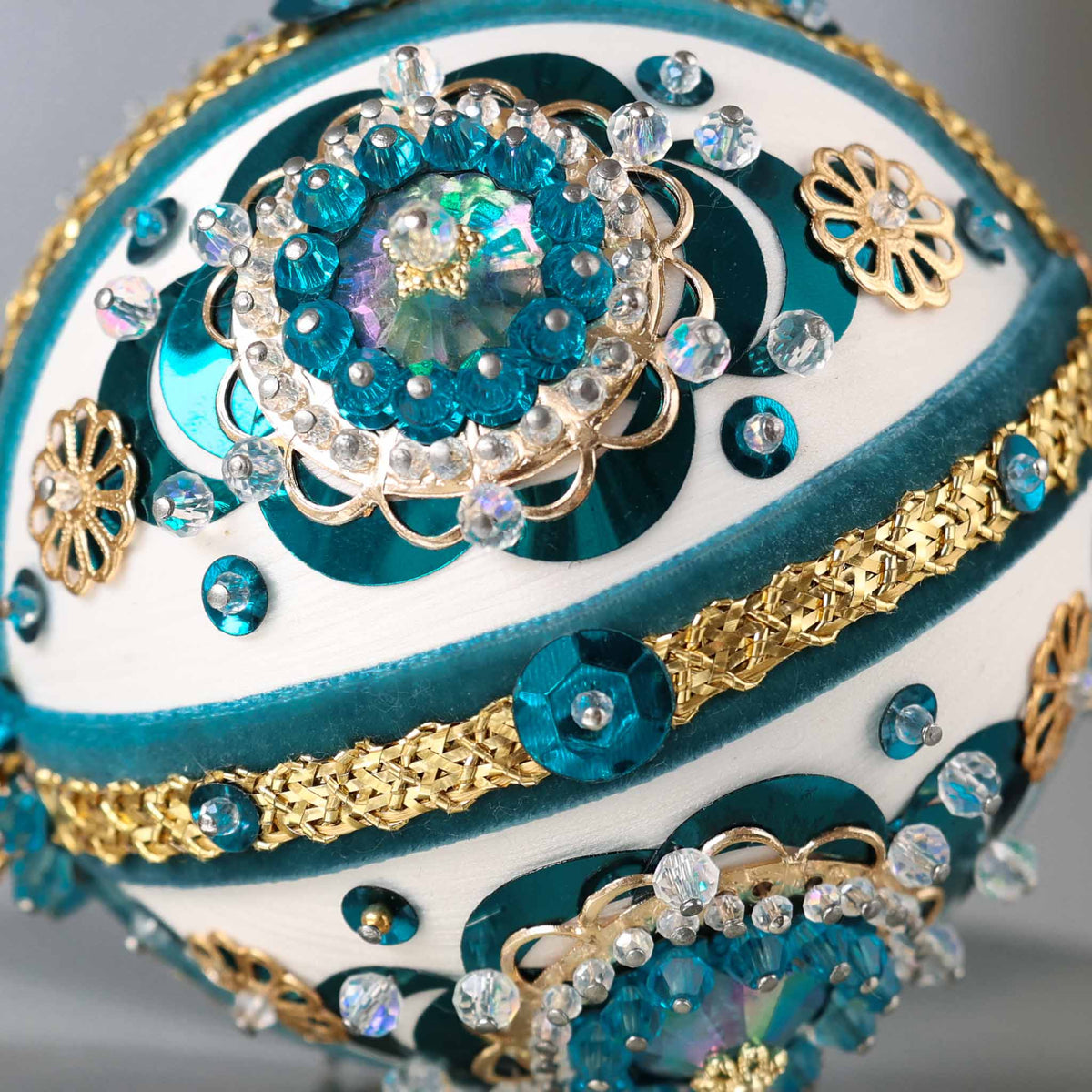 Close up of a handmade vintage 1970 Christmas beaded ornament featuring large plastic AB rhinestones, gold trim, and blue sequins, pinned to a satin core with dressmaker pins by Whim5seasons.
