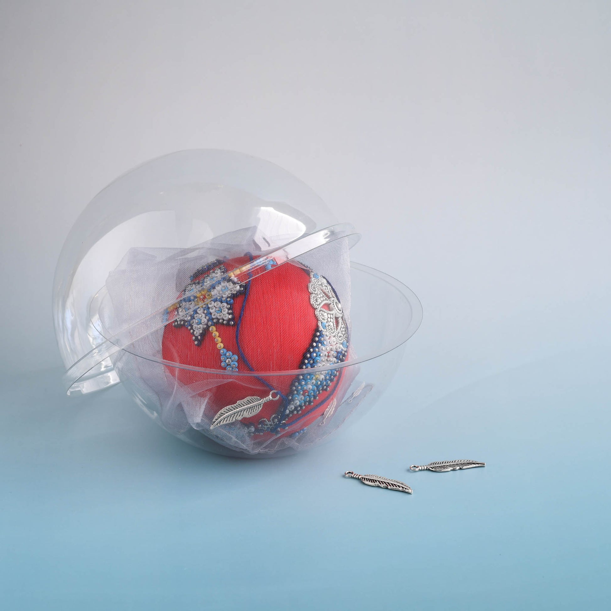 Handcrafted Christmas push pin ornament ball with silver charms in a clear plastic storage container on a light blue background by Whim5seasons.