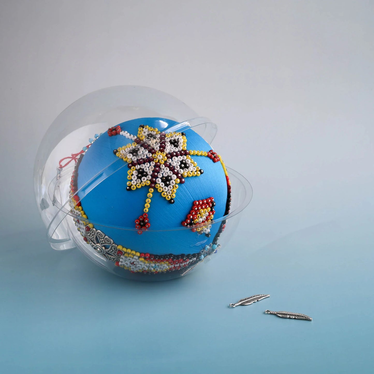 Decorative beaded ball with star design, inspired by indigenous art and patterns on a light blue background by Whim5seasons.
