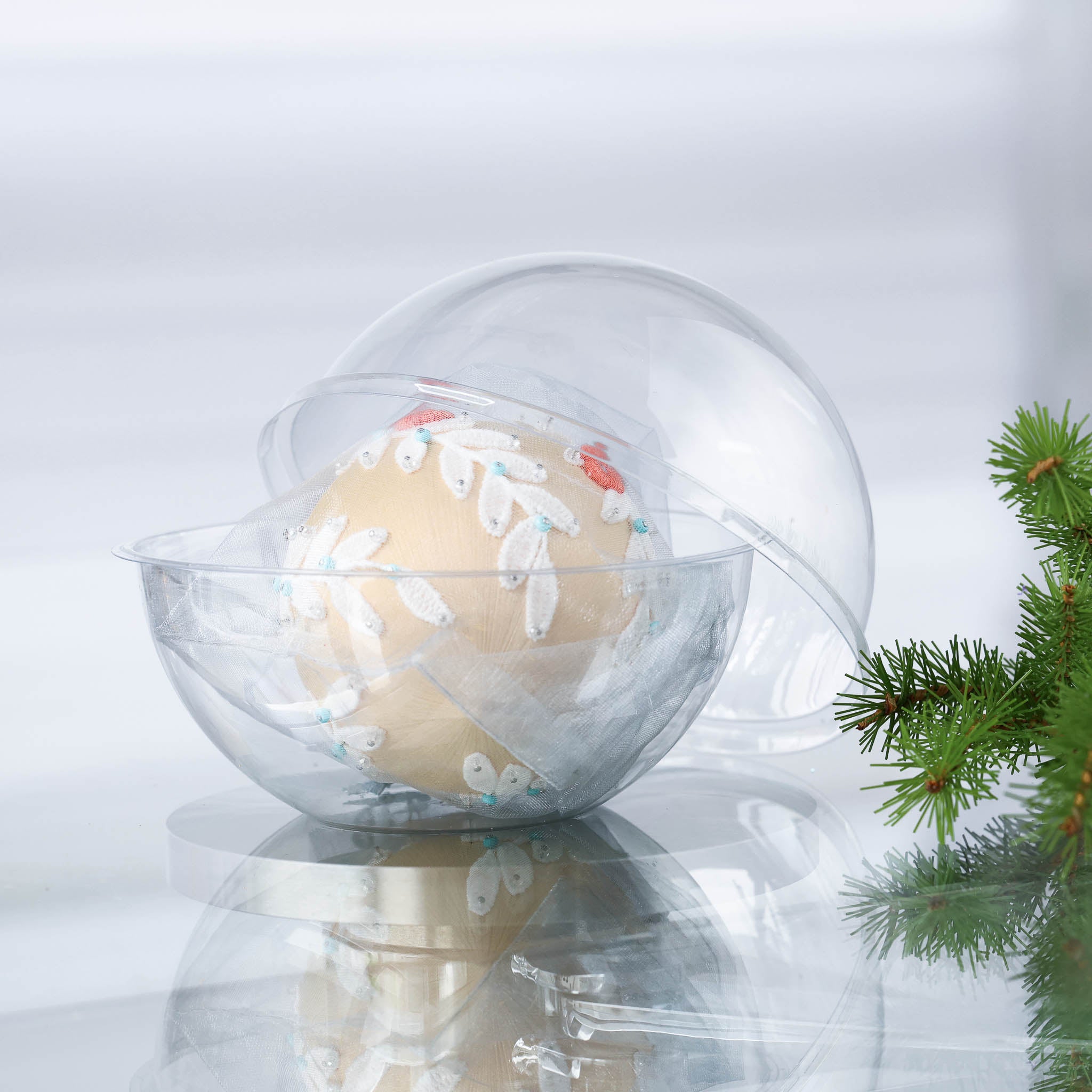 Handmade completed Frosted Laurel Satin Ornament in a clear plastic container with holiday Christmas greenery on a white background. (Papaya)