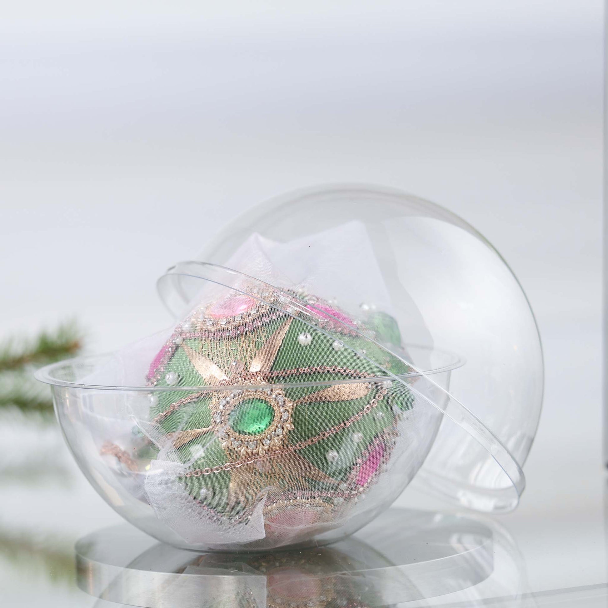 Decorative green satin Christmas ball with green and pink colors under a clear dome of a storage box on a white background by Whim5seasons. (Olive)
