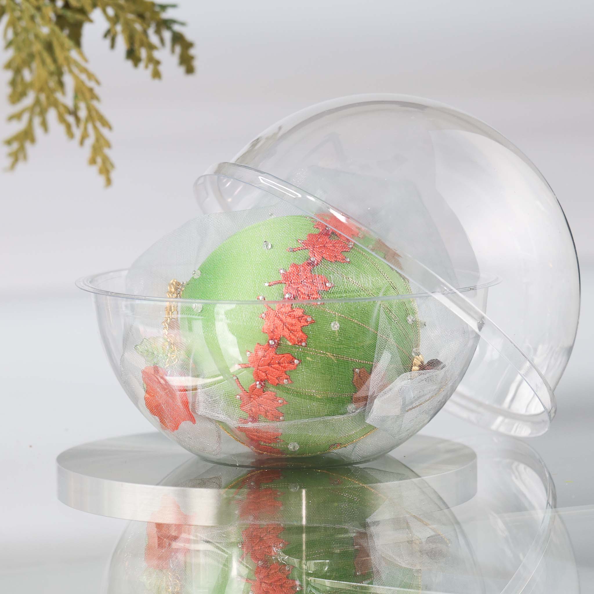 Completed Push Pin Ornament "Leaves Are Falling" features an olive colored satin foam core and comes in a gauze bag and a clear plastic storage container, pictured on top of the reflective surface. (Olive)