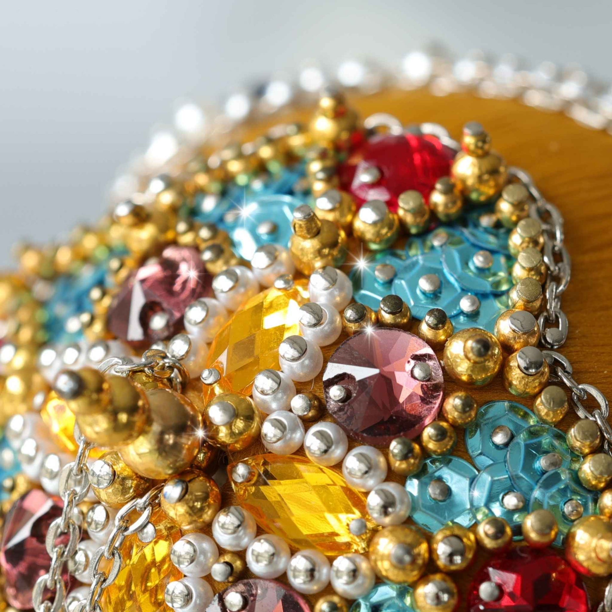A close-up of an ornate, heavily embellished Christmas Mid Century Style Handmade Ornament featuring large faceted gemstones in turquoise blue, surrounded by rows of pearls and metallic gold beads with silver chain details by Whim5seasons.