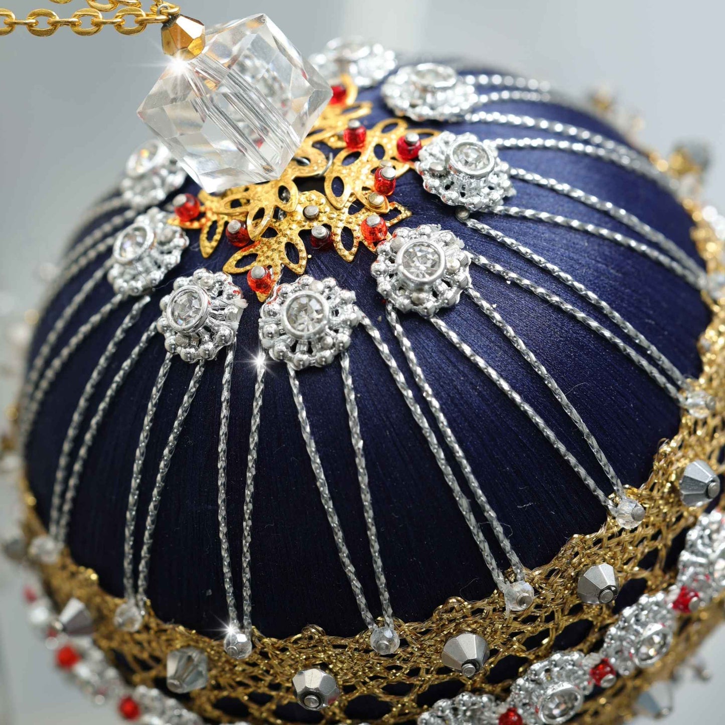A close-up detail of a handmade satin push pin ornament featuring  silver flower trim. large square clear glass bead, rows of silver bicone beads, and silver cord with dressmaker pins by Whim5seasons.