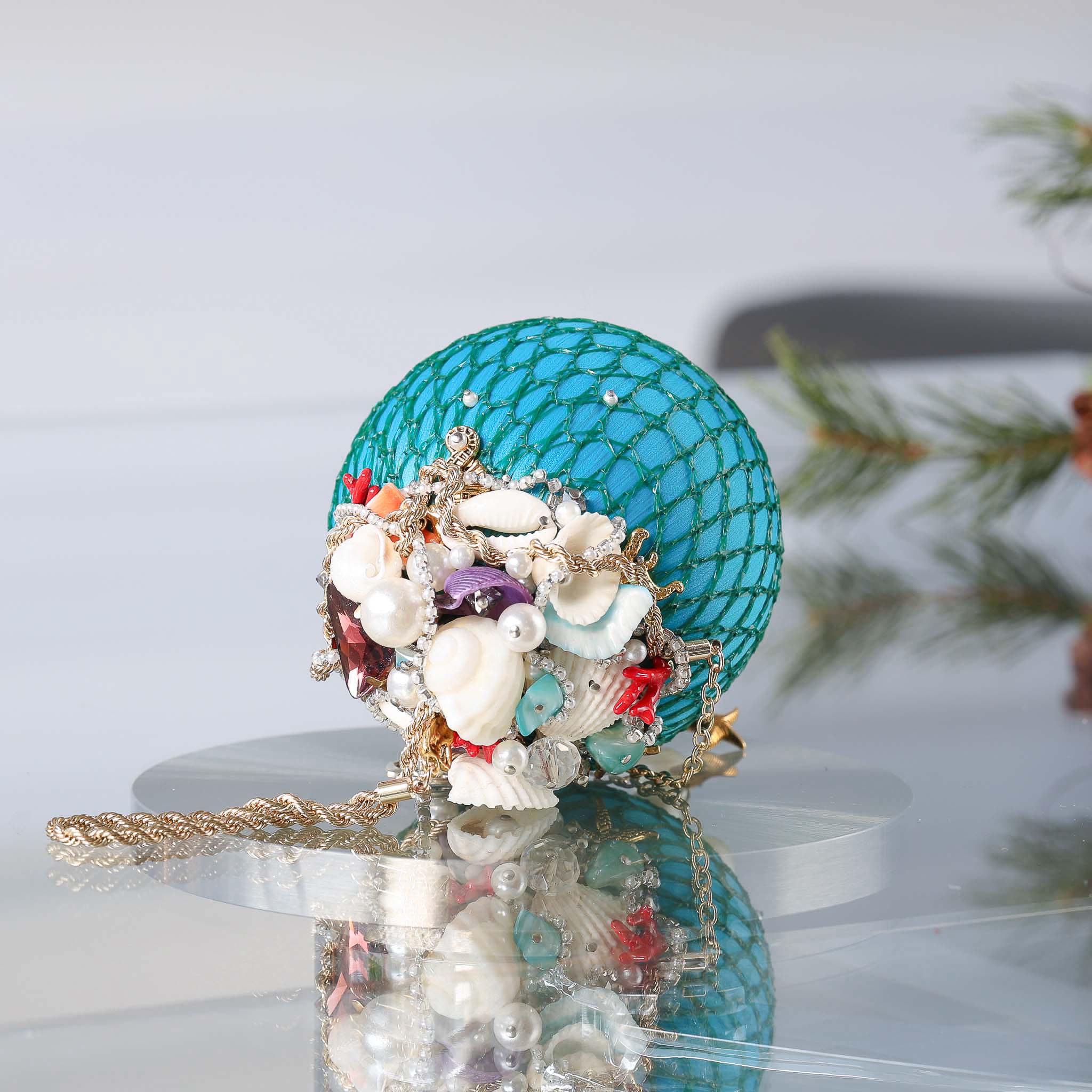 Close-up of a decorative teal push pin satin ball wrapped in mesh showing small beads, and real shells pinned with dressmaker pins by Whim5seasons.