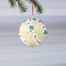 Handmade push pin beaded Christmas Ornament Ball embellished with embroidered flowers, white lace trim, and small clear beads hanging from a green evergreen branch. (Khaki)