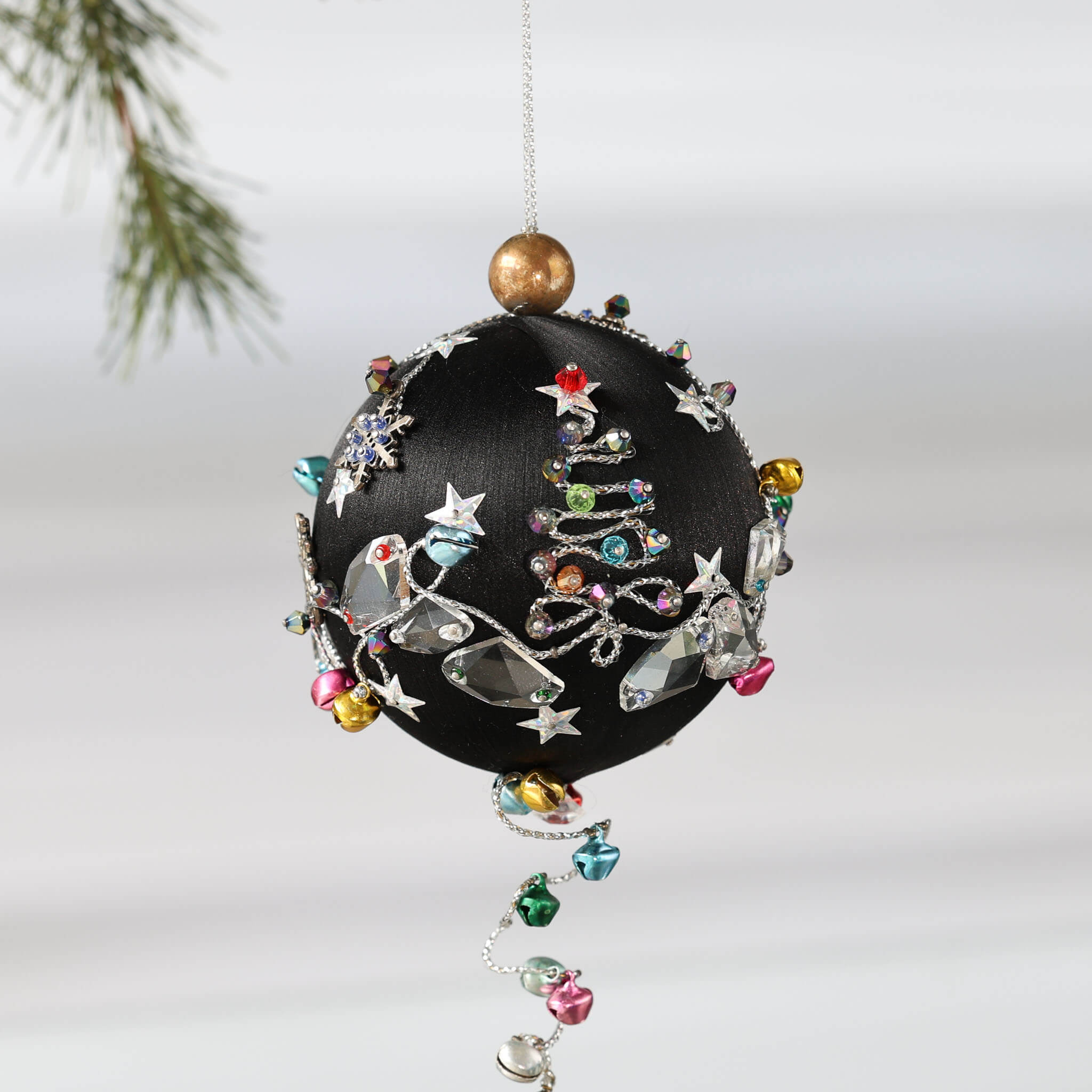 Handmade Christmas Satin Push Pin Ornament in black with large clear glass beads, silver snowflake, and tiny jingle bells  on a white background with a green evergreen branch.