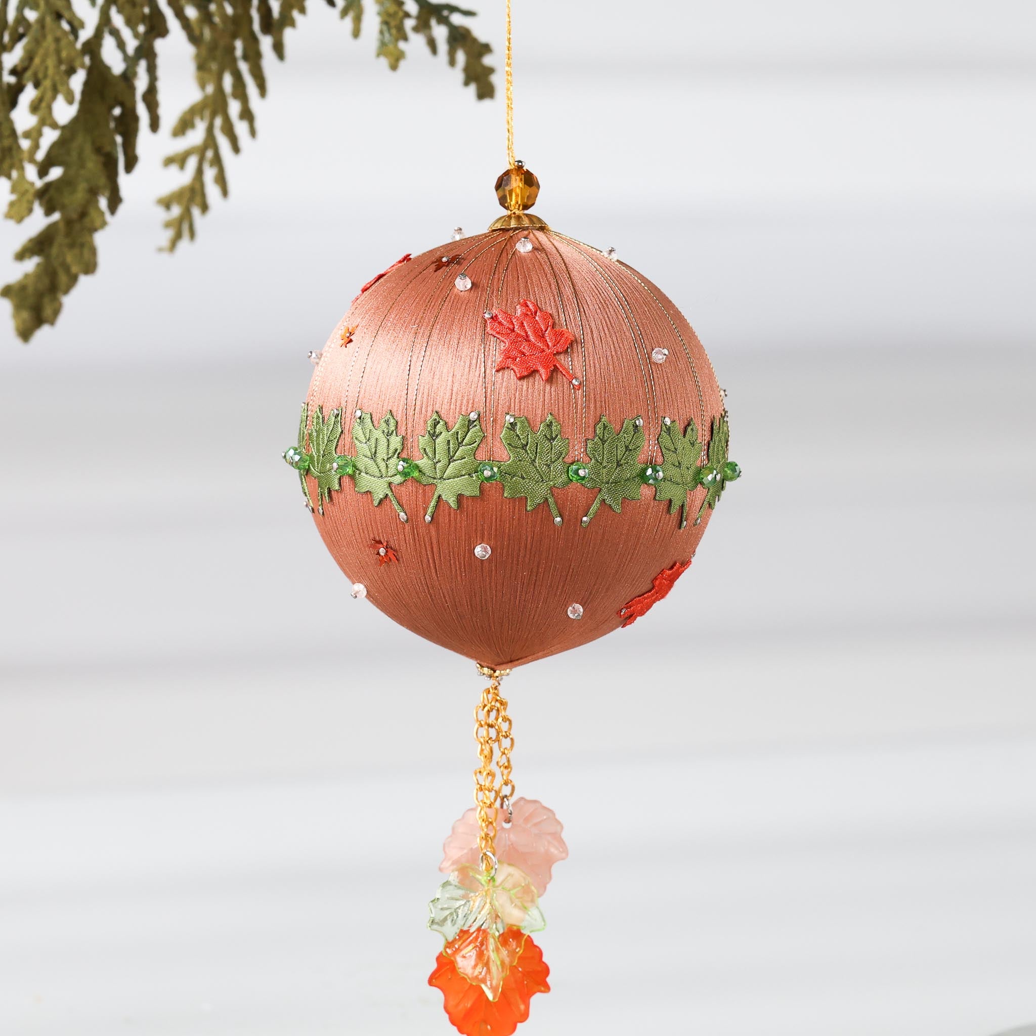A Handmade Push Pin Ornament in brown color featuring a green maple ribbon trim pinned to a satin foam core with dressmaker pins, and some acrylic maple leaf charms, and clear seed beads. (RosyBrown)