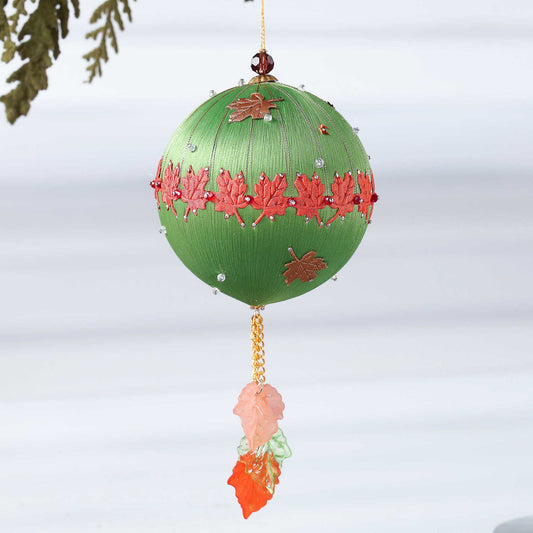 A Handmade Push Pin Ornament in olive featuring a rust colored maple ribbon trim pinned to a satin foam core with dressmaker pins, and some acrylic maple leaf charms, and clear seed beads. (Olive)