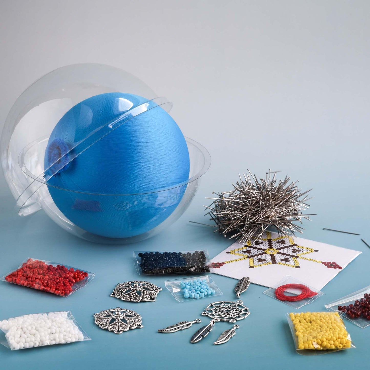 4" sky blue satin ball, clear container, beads, alloy charms, and pins on a blue surface - materials for a DIY push pin ornament project by Whim5seasons.