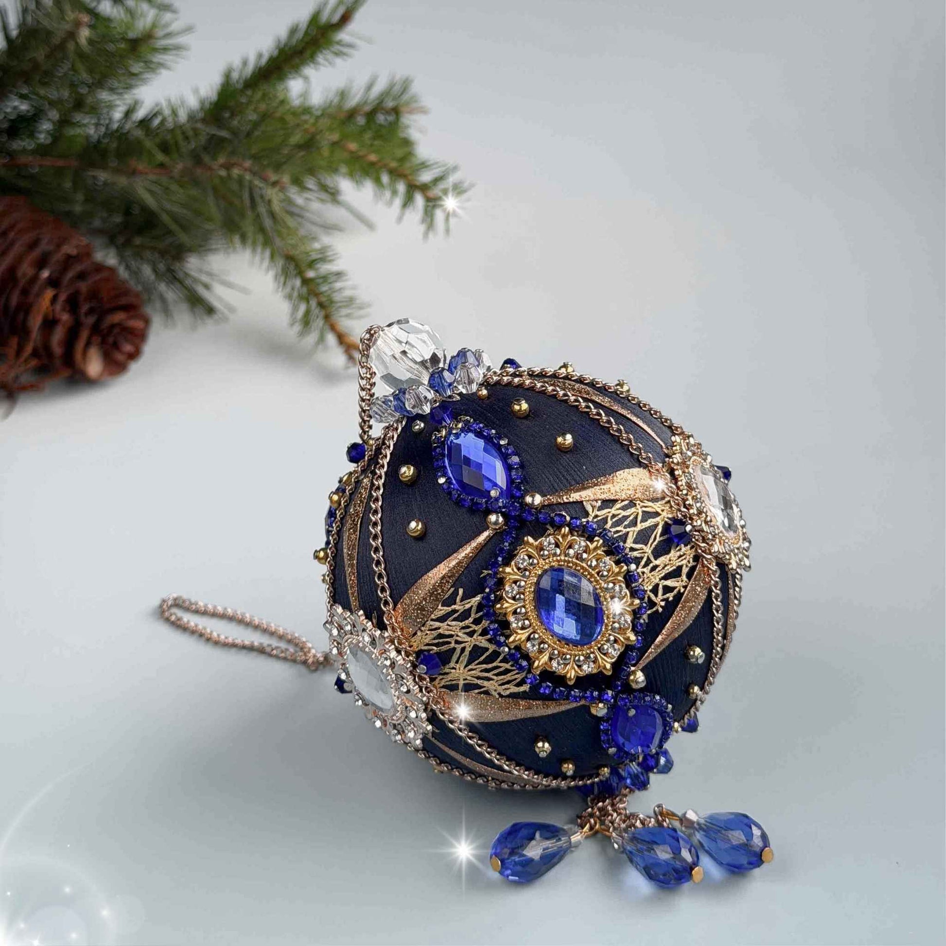 Decorative handmade dark blue push pin Christmas ornament with blue and gold details on a light blue background with an evergreen branch by Whim5seasons.