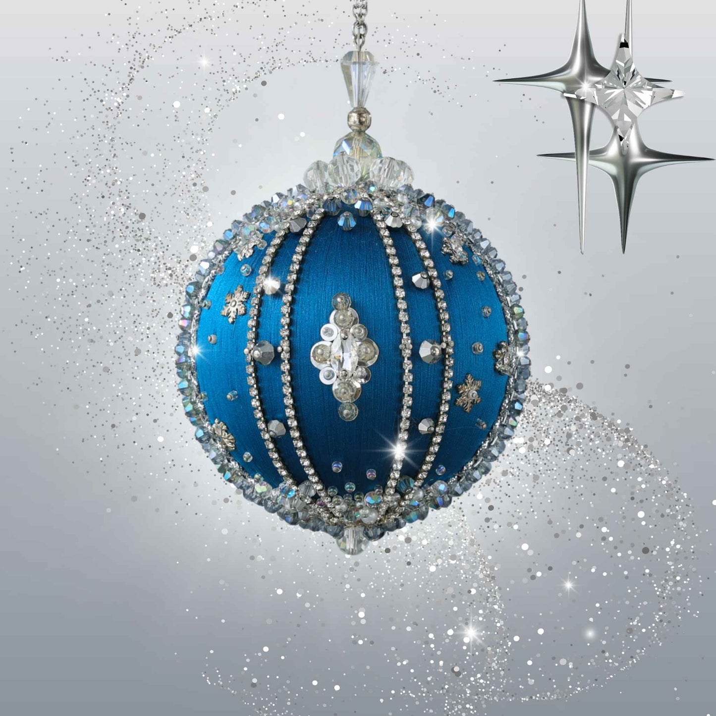 A decorative Christmas ornament featuring a satin blue ball embellished with silver rhinestones, crystal details, and snowflake motifs, shown against a sparkling silver and gray background with star accents by Whim5seasons.