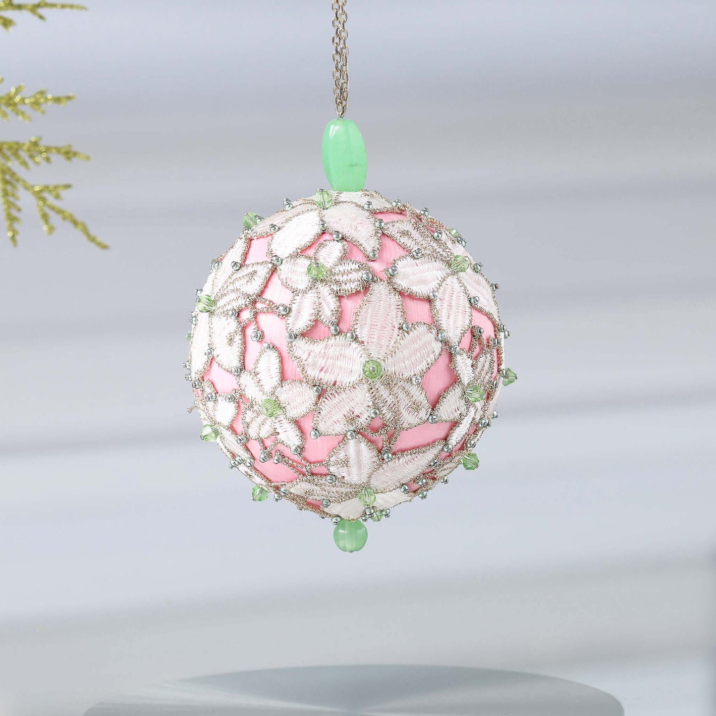 Handmade sequin & beaded pink satin ornament featuring flower trim hanging in front of gray background and holiday greenery by Whim5seasons.