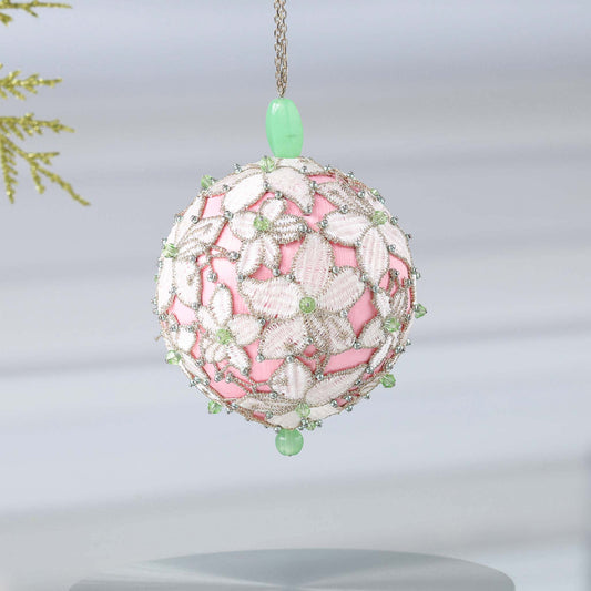 Handmade sequin & beaded pink satin ornament featuring flower trim hanging in front of gray background and holiday greenery by Whim5seasons.