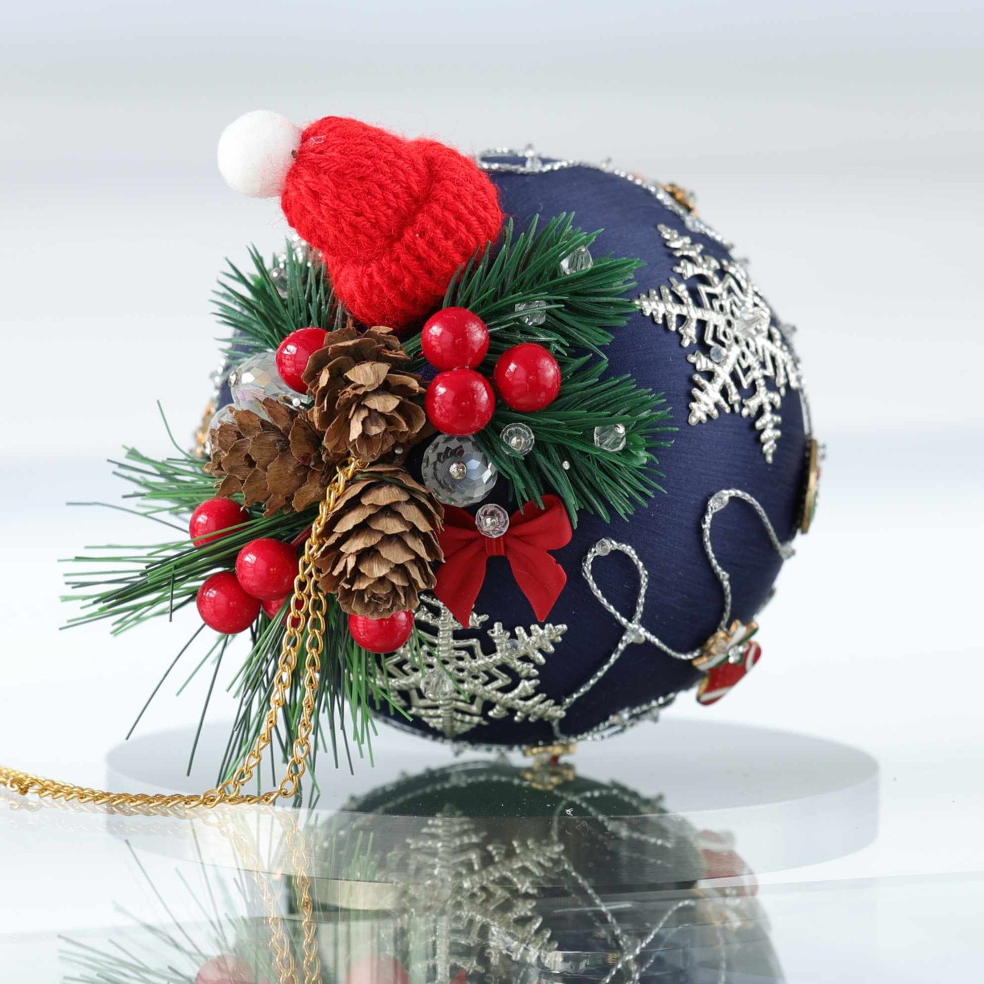 Handmade Christmas satin ball with cute knit red hat, pine cones, and berries on a white background by Whim5seasons.