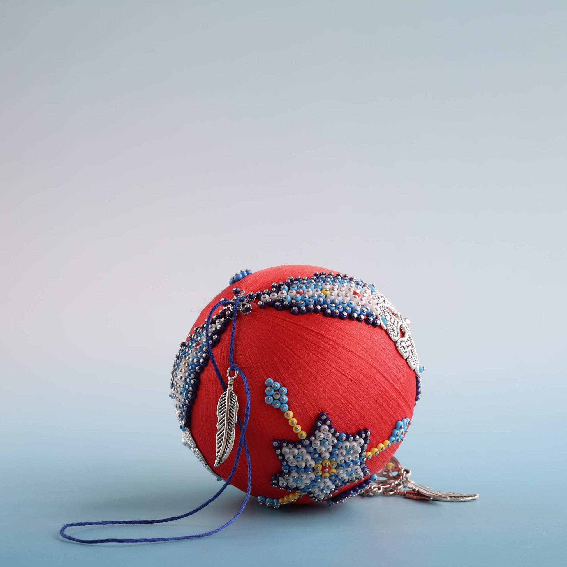 Decorative red ball with indigenous style beadwork and a dream catcher charm on a light blue background by Whim5seasons.