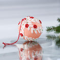 Load image into Gallery viewer, Handmade push pin beaded Christmas Ornament Ball embellished with embroidered flowers, white lace trim, and small clear beads on a reflective surface with holiday greenery. (Coral)
