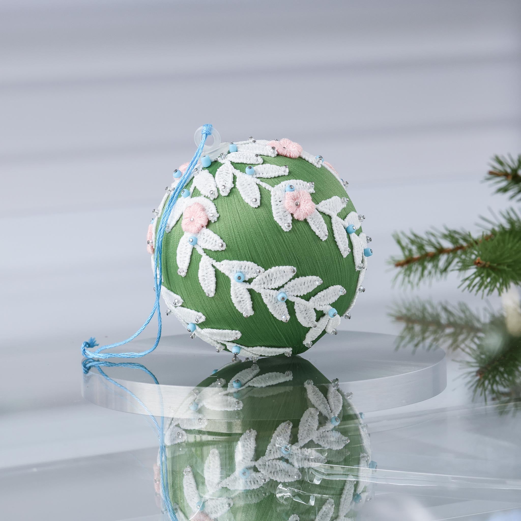 Handmade olive green Christmas or Easter Beaded push pin Ornament Ball embellished with flowers, white trim, and beads on a reflective surface with holiday greenery. (Olive)