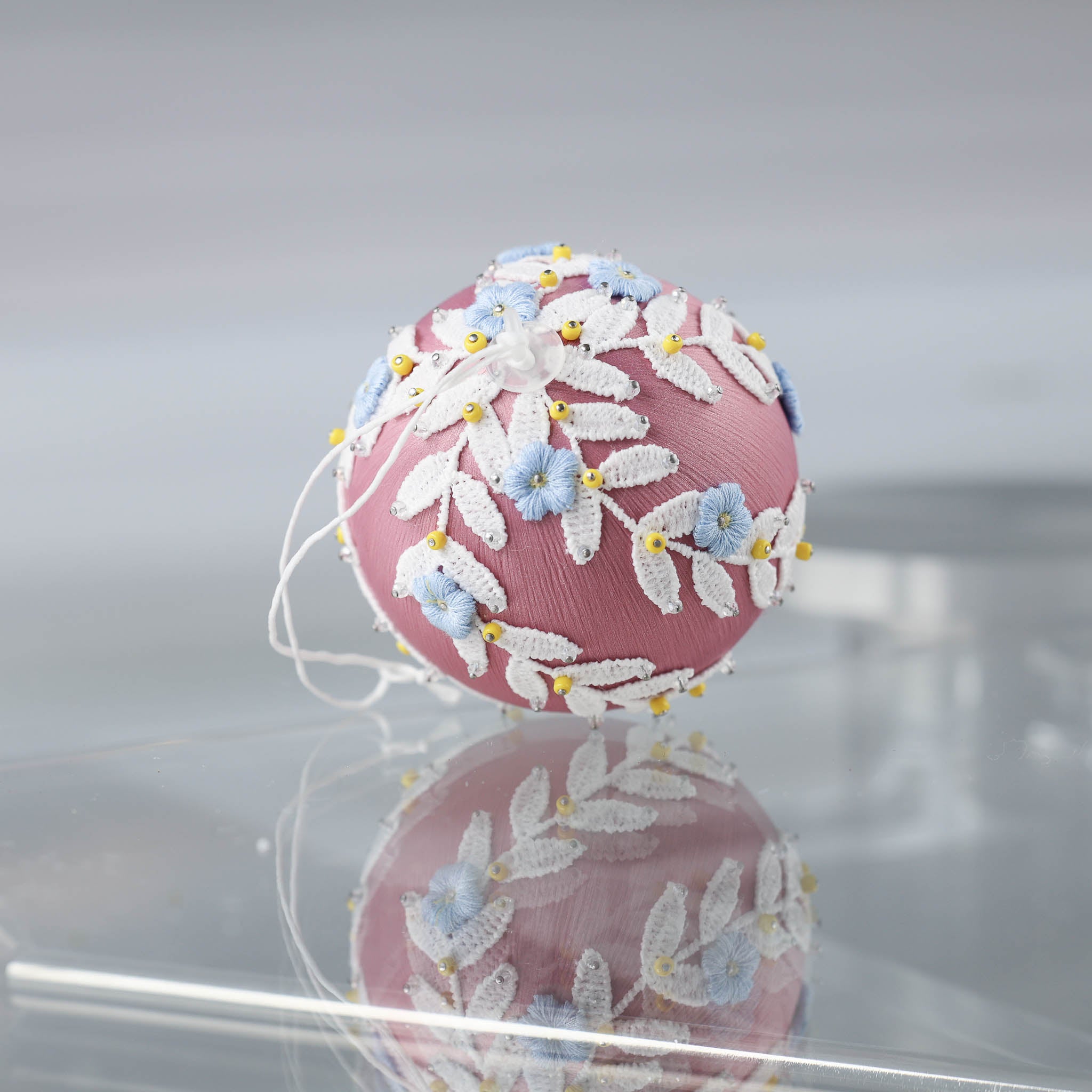 Handmade Christmas or Easter Beaded push pin Ornament Ball with blue embroidered flower patches, white trim, and beads pinned to a satin foam core on a light gray background.  (Pale Violet Red)
