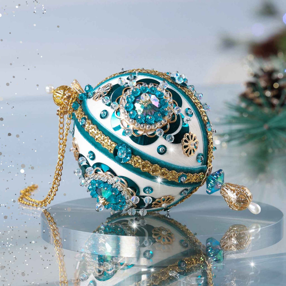 Handmade 1970 retro mid century white satin push pin ornament featuring large AB rhinestones, blue crescent sequins, and a filigree gold bead on the bottom with a Christmas branch in the background by Whim5seasons.