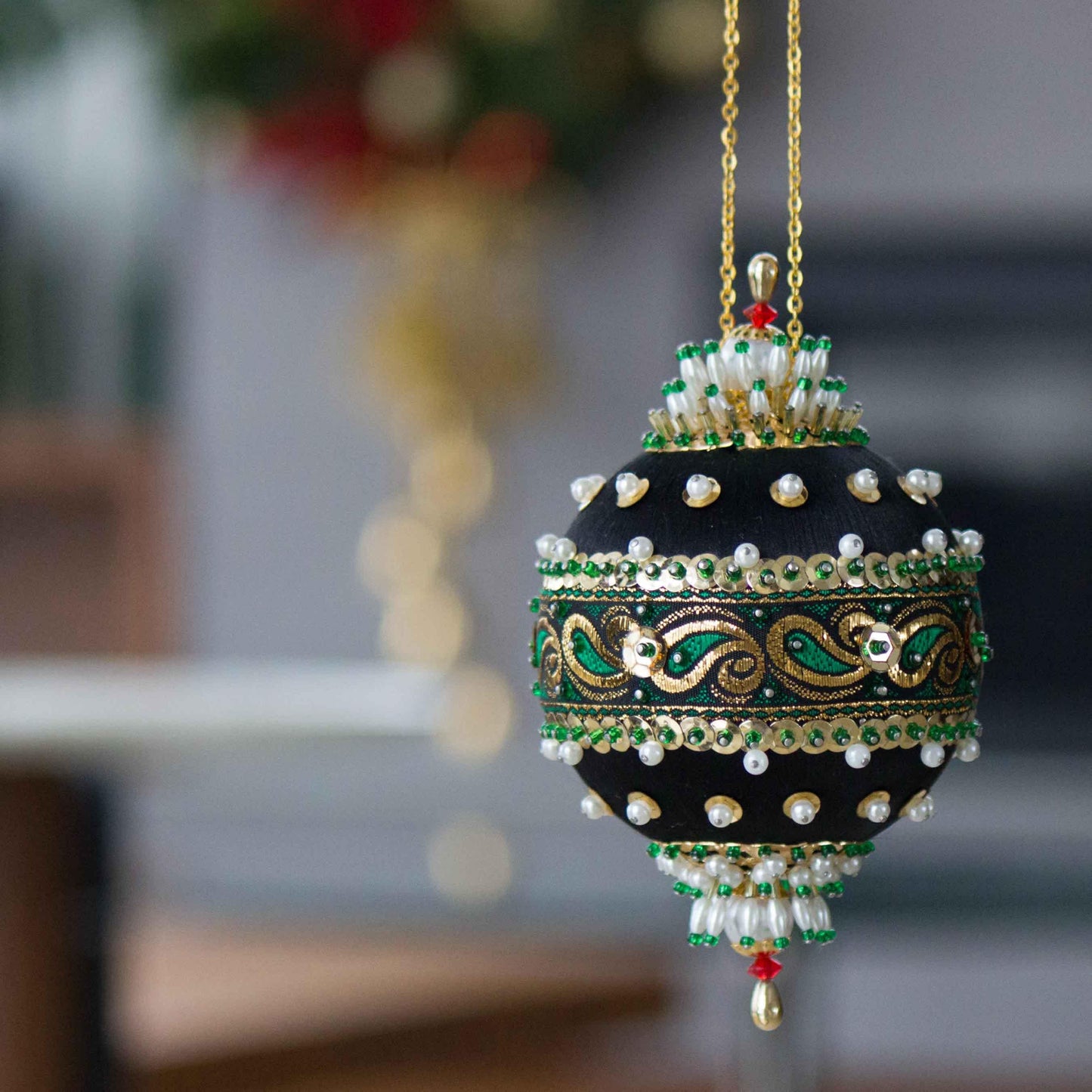 Handmade 1970 mid century black satin push pin ornament featuring pearls beads  and gold sequins, hanging on a gold chain, with a Christmas wreath in the background by Whim5seasons.