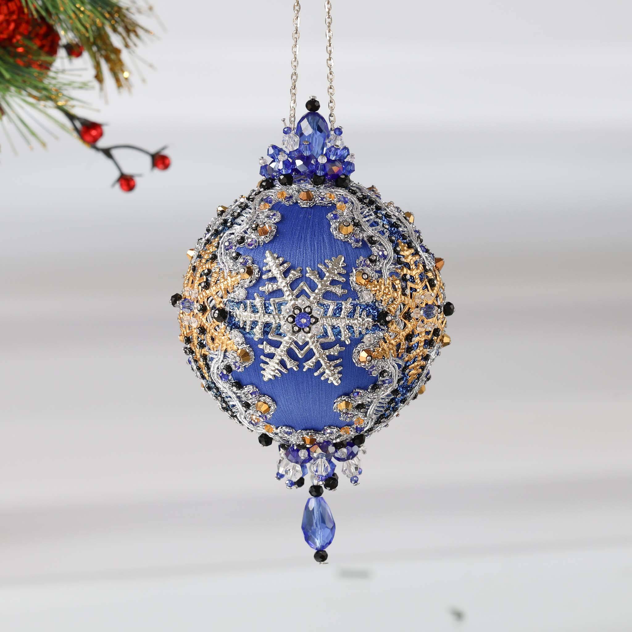 Handmade Christmas Satin Ornament with clear glass beads, silver snowflake, and a silver chain on a white background with a green holiday branch. (Blue)