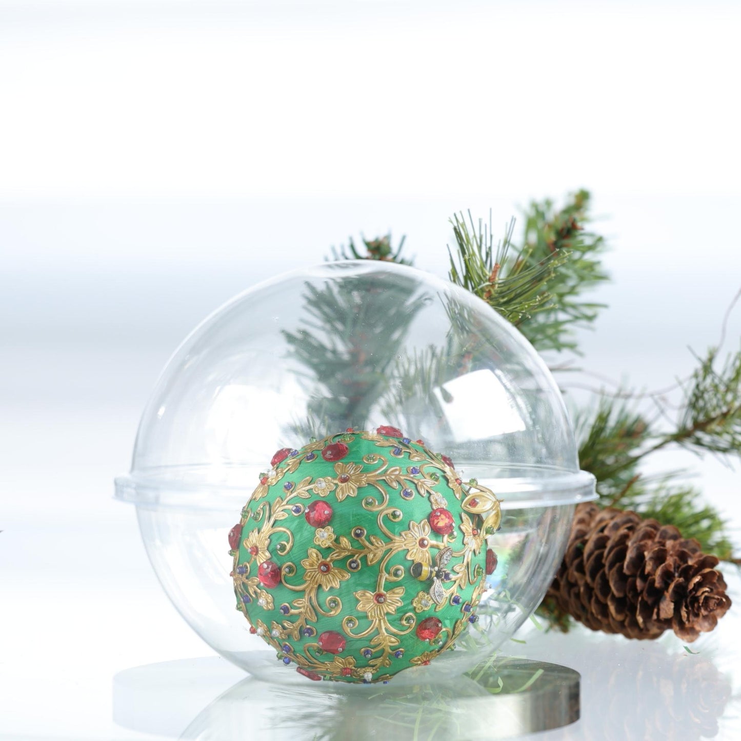 Decorative handmade Christmas satin ball with gold and red details inside a clear glass storage container, surrounded by pine branches and a pine cone by Whim5seasons.