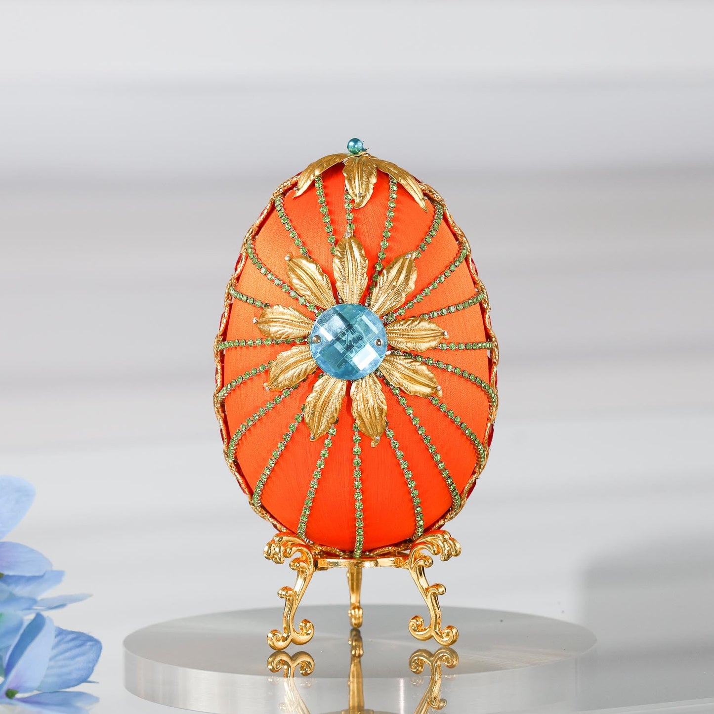 A handmade large Easter egg push pin ornament with a large gold flower on a gold stand on a reflective surface by Whim5seasons.