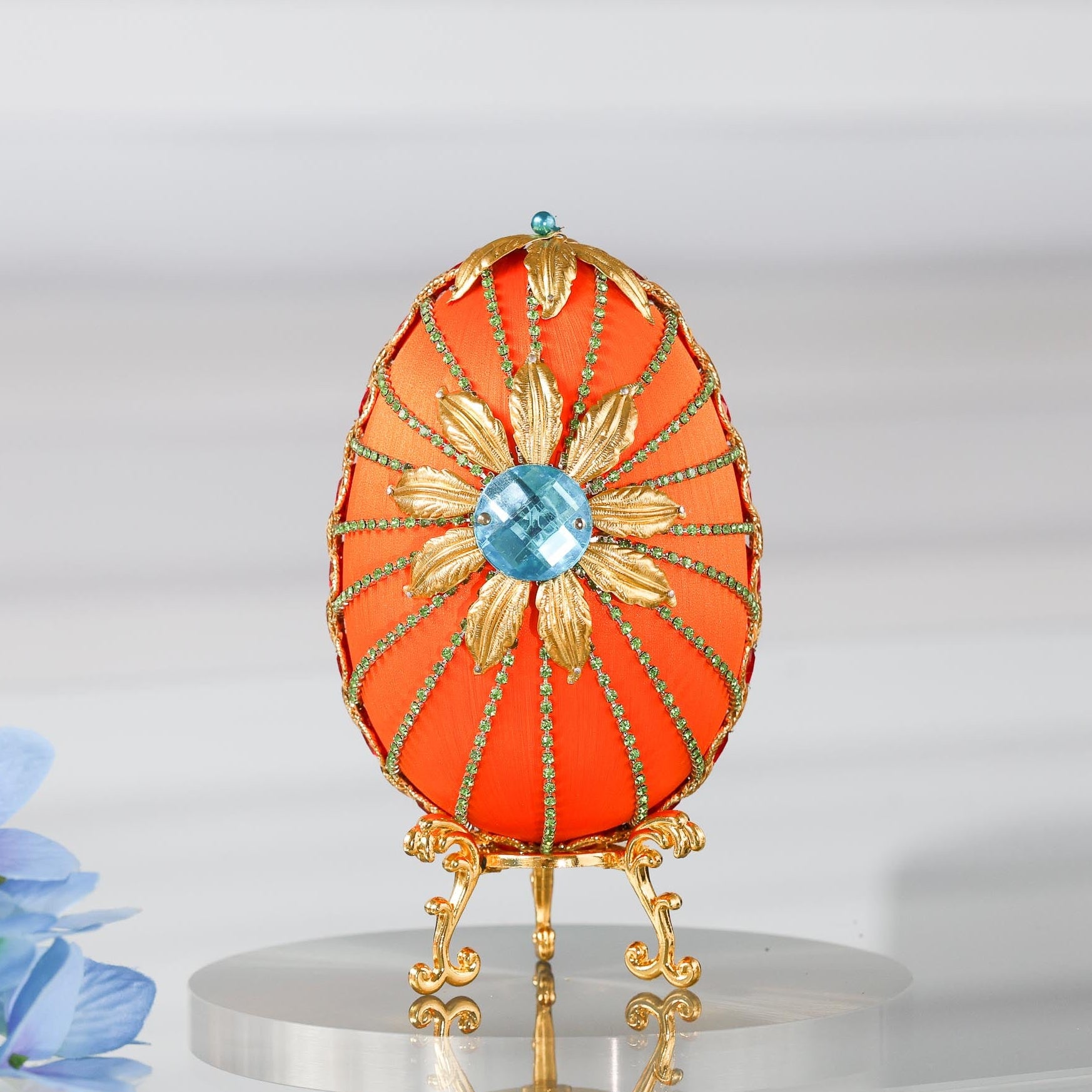 A handmade large Easter egg push pin ornament with a large gold flower on a gold stand on a reflective surface by Whim5seasons.