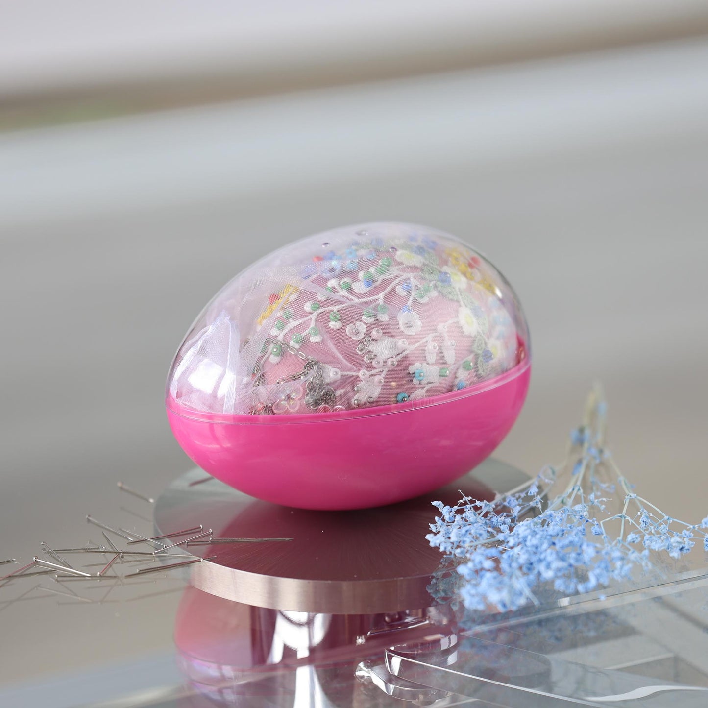 Handmade Push Pin Easter Egg Ornament with floral embroidery inside a green storage container on a reflective surface by Whim5seasons.