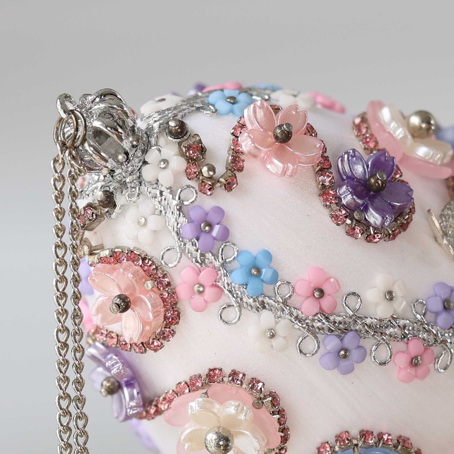 A close-up detail of a handmade Easter egg push pin ornament featuring small silver crown and pastel acrylic flower charms by Whim5seasons.