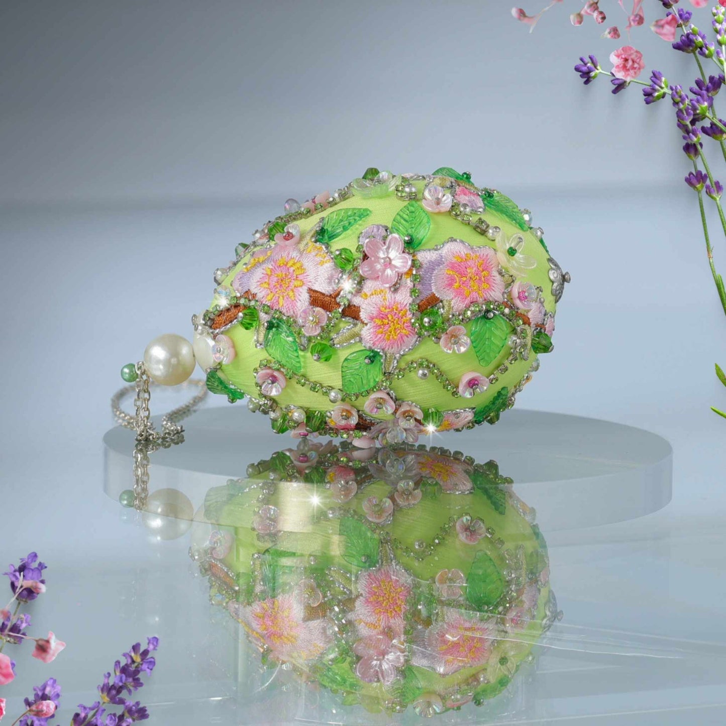 Close up of a handmade Easter Egg Push Pin Ornament embellished with crystals, beads, and metallic trim on a gray background with large pearls by Whim5seasons. 