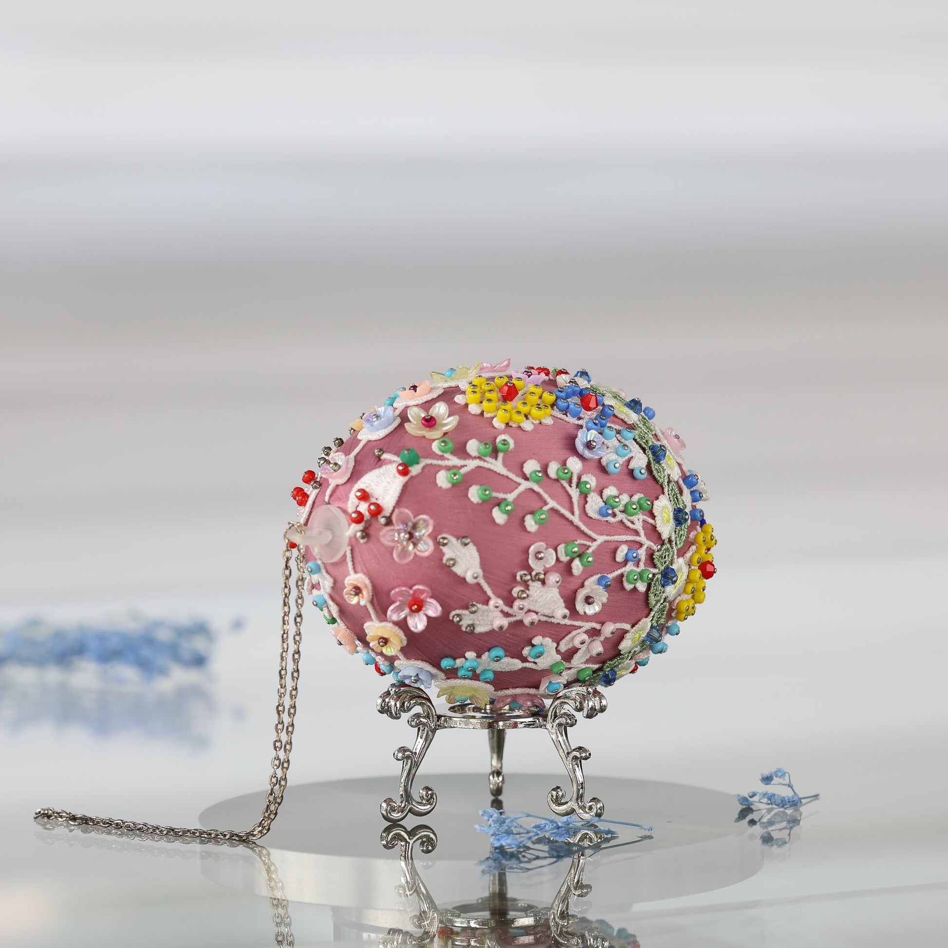 Large 4 inch mauve Easter egg push pin ornament on a silver stand on a reflective surface featuring white lace and seed beads embellishments by Whim5seasons.