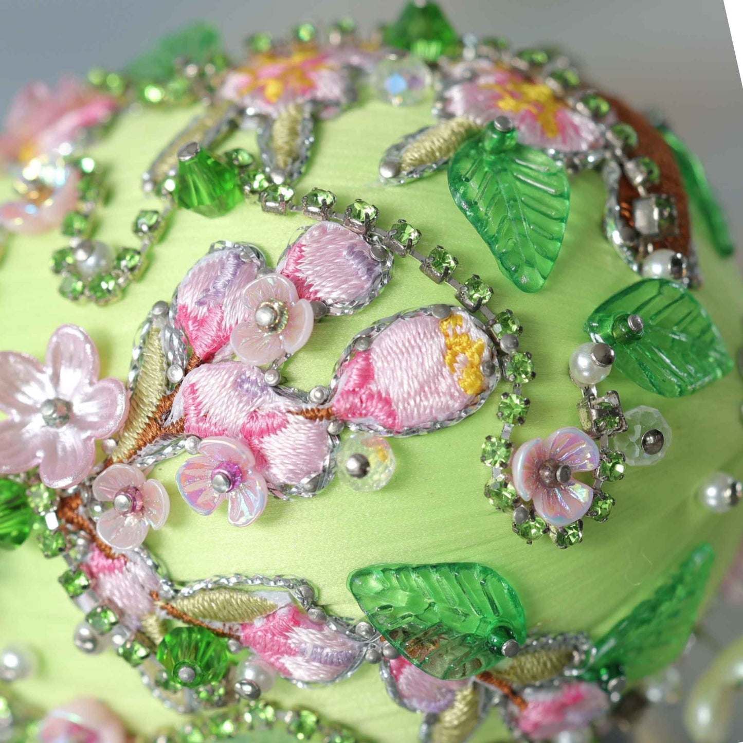 Close up of a handmade Easter Egg Push Pin Ornament embellished with tiny pink flowers and embroidered patches resembling Faberge style egg on a gray background by Whim5seasons.