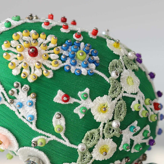 A close-up detail of a small green Easter egg push pin ornament showing blue seed beads pinned with dressmaker pins to the satin core.